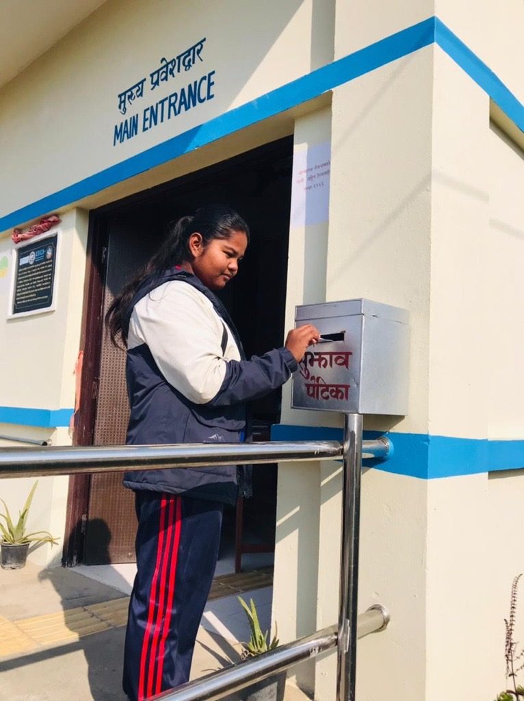 Mira is standing in front of a door and putting something in a box