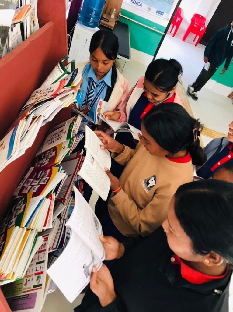 Mira with her friends reading book placed in book shelves.
