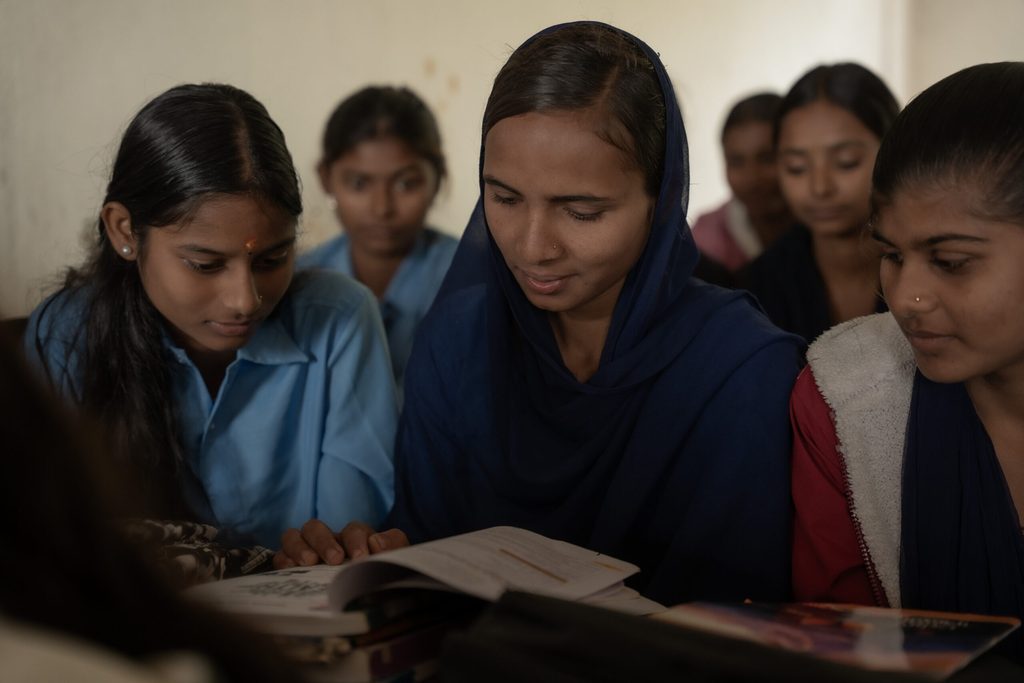 Three girls in the classroom wearing school uniform and reading text books.