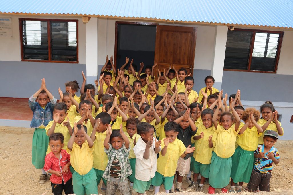 Group of young school children waving their arms in the air.
