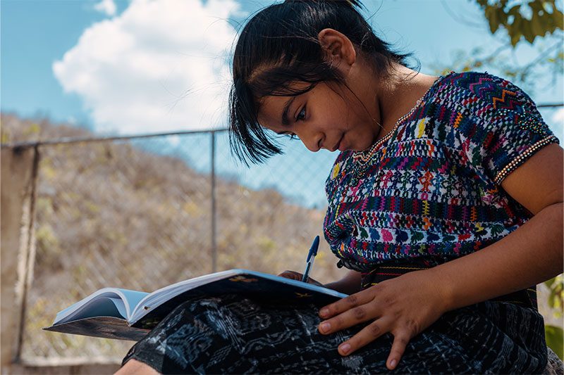 Niña de comunidad en Guatemala escribiendo y sonriendo.