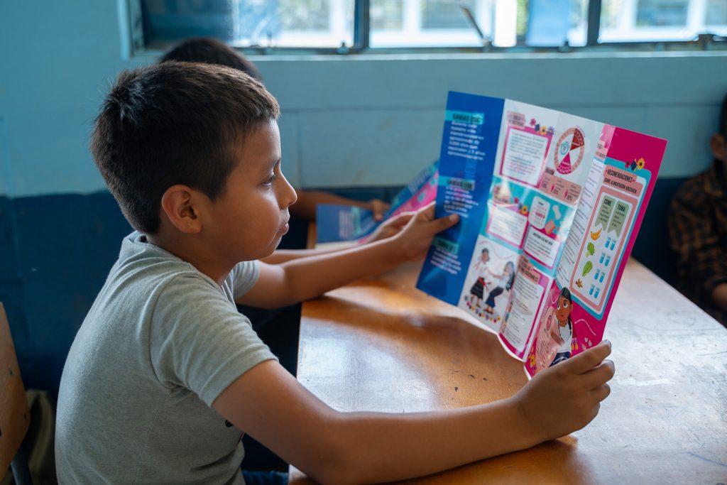 Niño leyendo un folleto sobre higiene menstrual con atención.