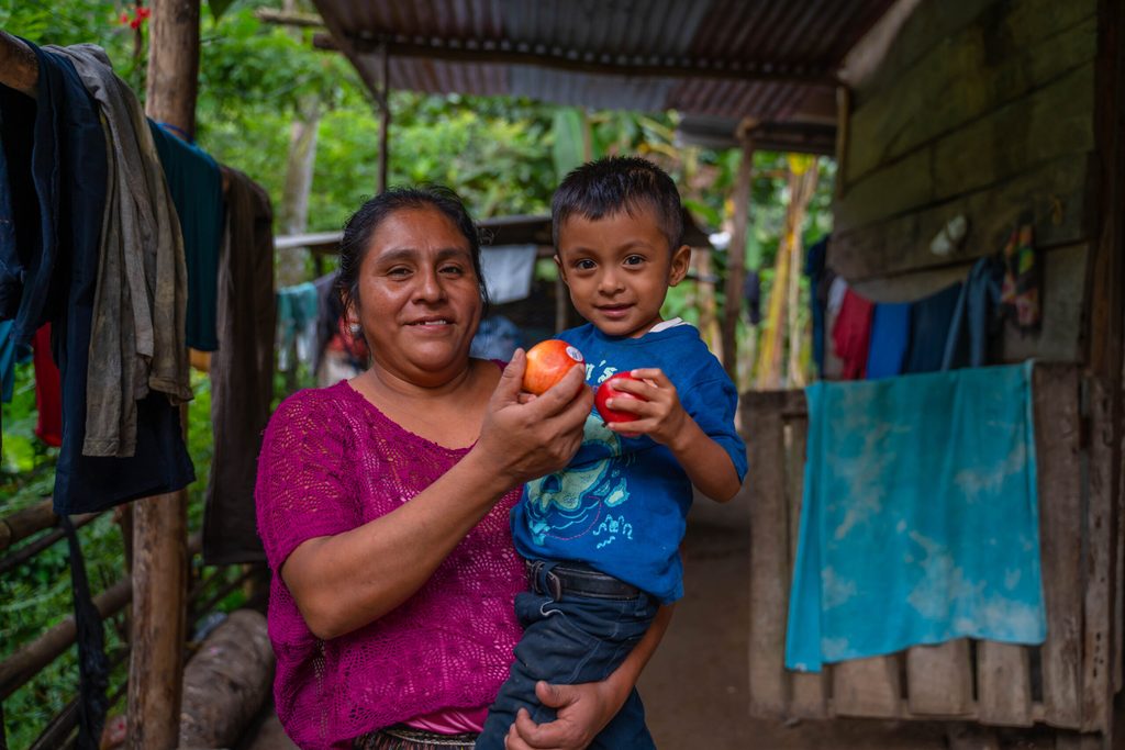 Mujer sostiene a su hijo pequeño mientras participan en una actividad humanitaria enfocada en la alimentación.