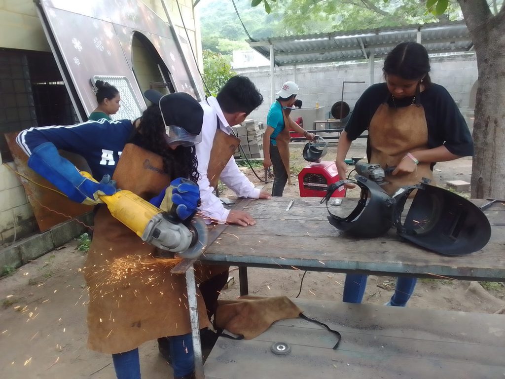 Jovenes mujeres y hombres en taller de soldadura.