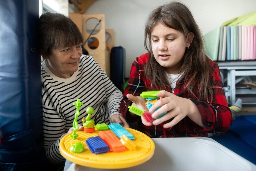 Alisia plays with an educational toy with one of the Patchwork association workers. 