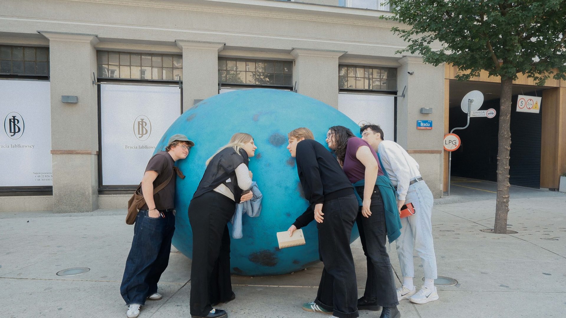 Group of people putting their ears to a statue of a blue egg making sounds. 