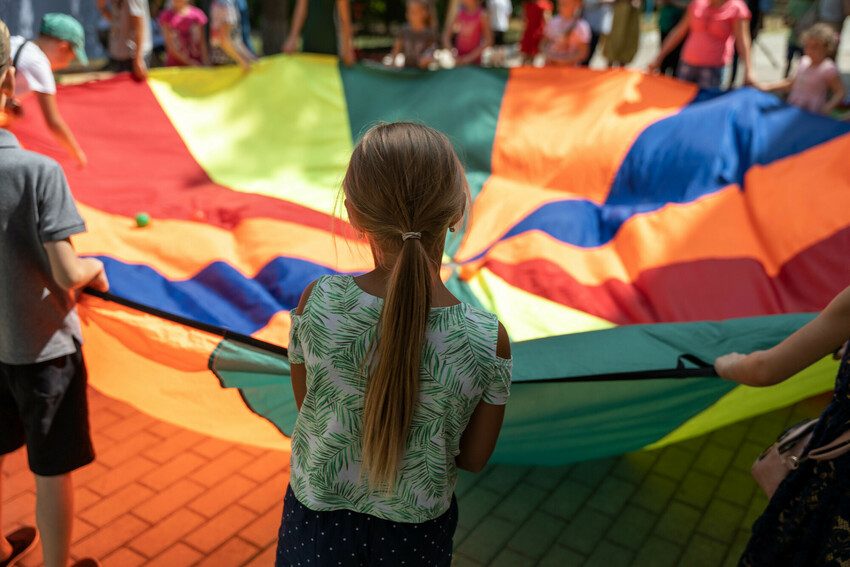 Lots of children hold the edge of a play parachute.