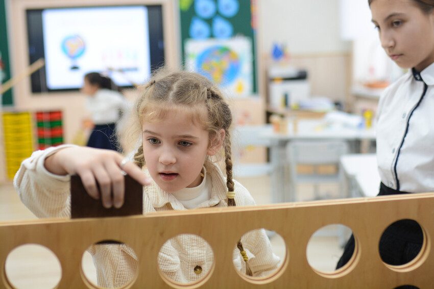 A girl slides a block into a large wooden toy. 